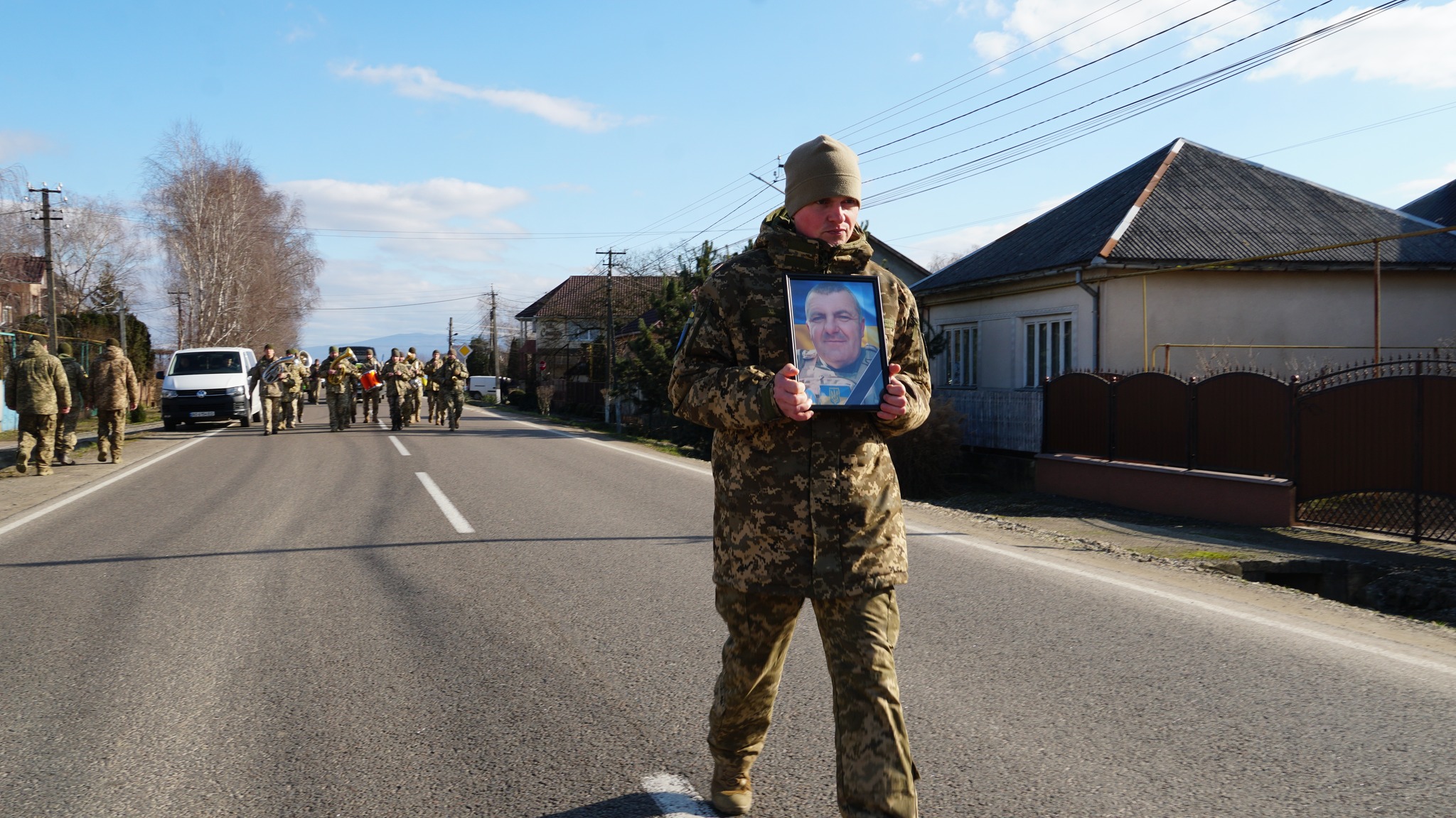 Військовий з портретом полеглого захисника на центральній вулиці його рідного села 