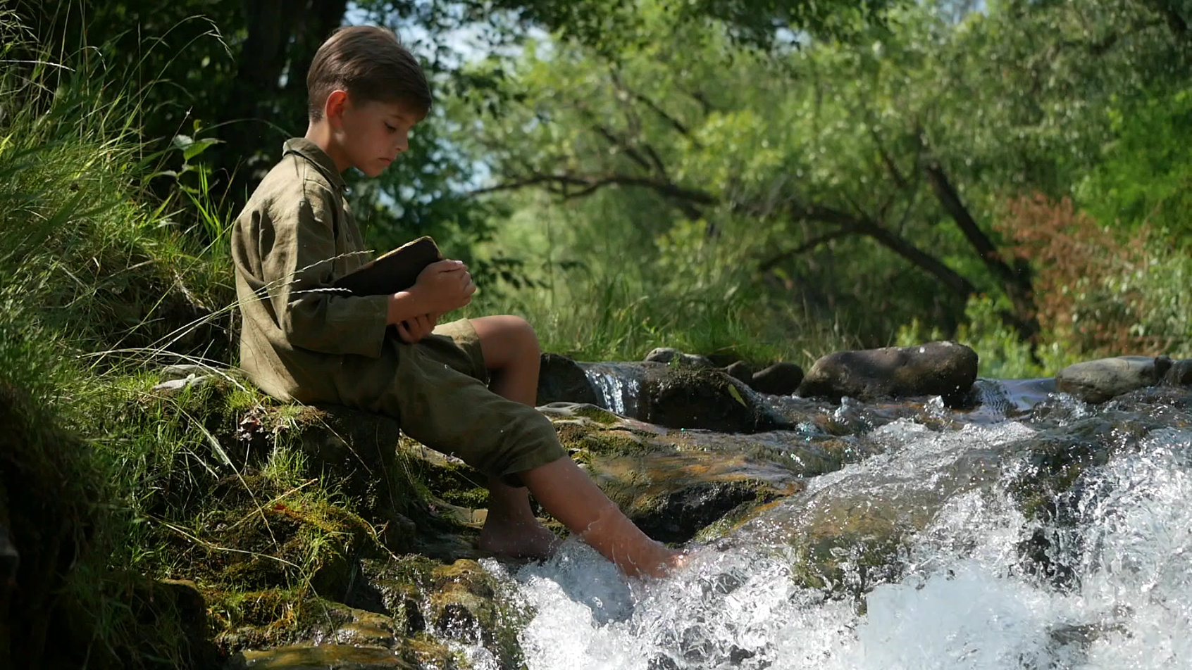 Хлопчик з книжкою на березі гірської річки