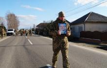 Військовий з портретом полеглого захисника на центральній вулиці його рідного села 